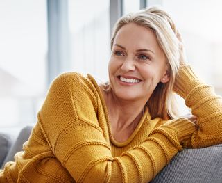 A woman wearing a yellow jumper smiling while sitting on a couch